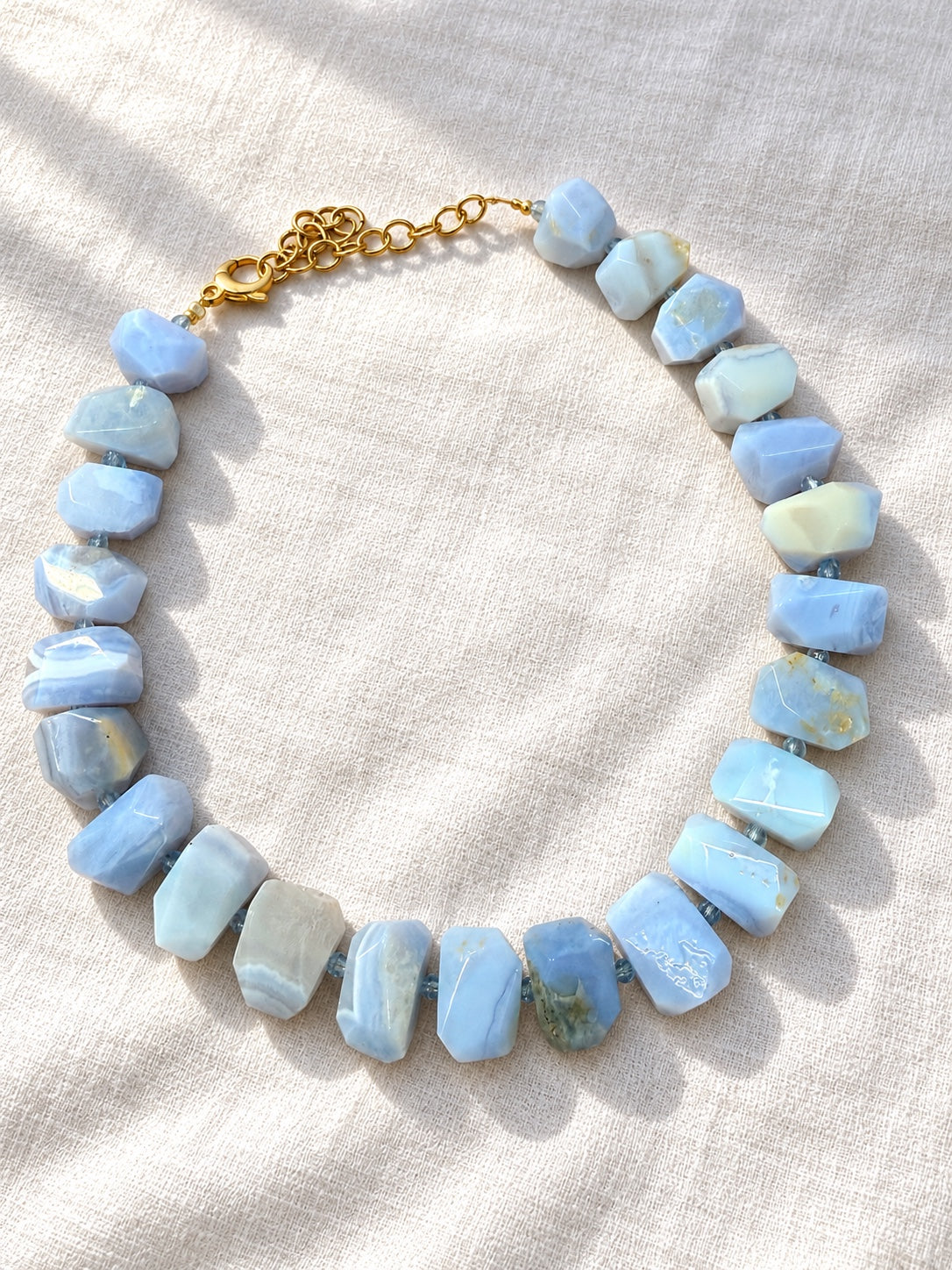 Collana Madre Terra con pietre sfaccettate di calcedonio azzurro e chiusura dorata su tessuto bianco